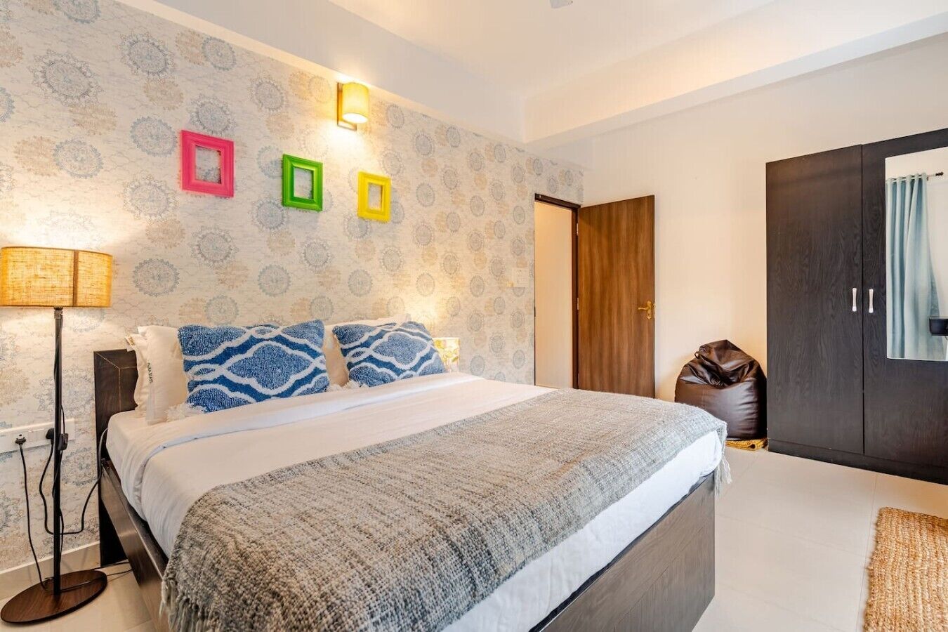 Quarto moderno com uma cama grande, abajur, guarda-roupa e parede com molduras decorativas.