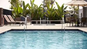 Ein Pool mit Liegestühlen und einem Tisch, umgeben von viel Grün.