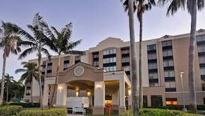 Un hôtel à plusieurs étages, doté d’une entrée principale, de palmiers et d’une pelouse bien entretenue.