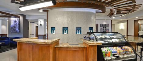 A reception area with a wooden counter, a glass display case with beverages, and a wall-mounted TV.
