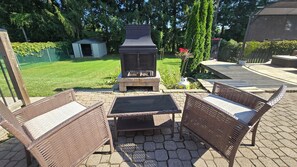 An outdoor patio with wicker furniture, a grill, and a small shed in a garden setting.