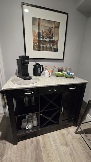 A kitchen counter with a coffee maker, a framed picture above, and a cabinet below. - The Thomas House ~ 2Br ~ Pet Friendly ~ Getaway (Cobourg)