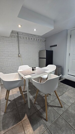 A modern dining area with a white brick wall, a table with chairs, and a refrigerator.