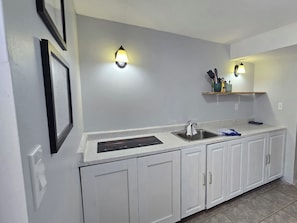 A kitchen with white cabinets, a stainless steel sink, a built-in range hood, and two wall-mounted light fixtures. - The Thomas House ~ 2Br ~ Pet Friendly ~ Getaway (Cobourg)