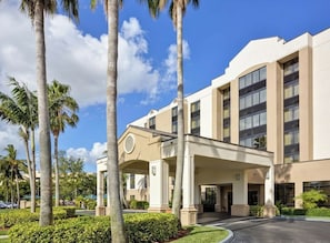 A hotel with a covered entrance, palm trees, and a clear sky.