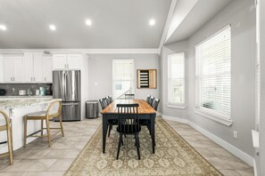 Eine moderne Küche mit weißen Schränken, einem Edelstahl-Kühlschrank und einem Essbereich mit Holztisch und Stühlen.