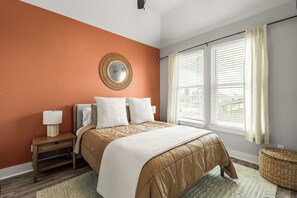 Un dormitorio con cama, mesitas de noche, un espejo y una ventana con cortinas.