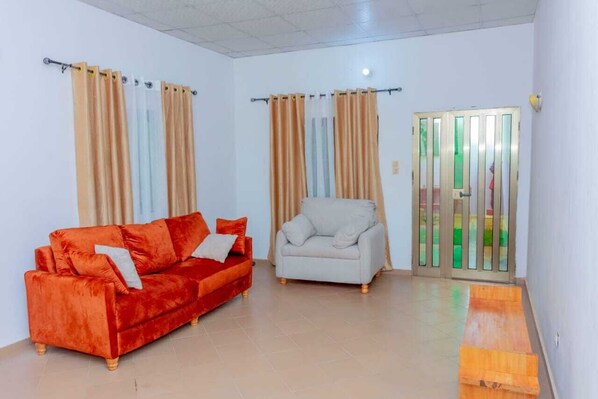 A room with a red sofa, a grey armchair, and a sliding glass door leading to an outdoor area.