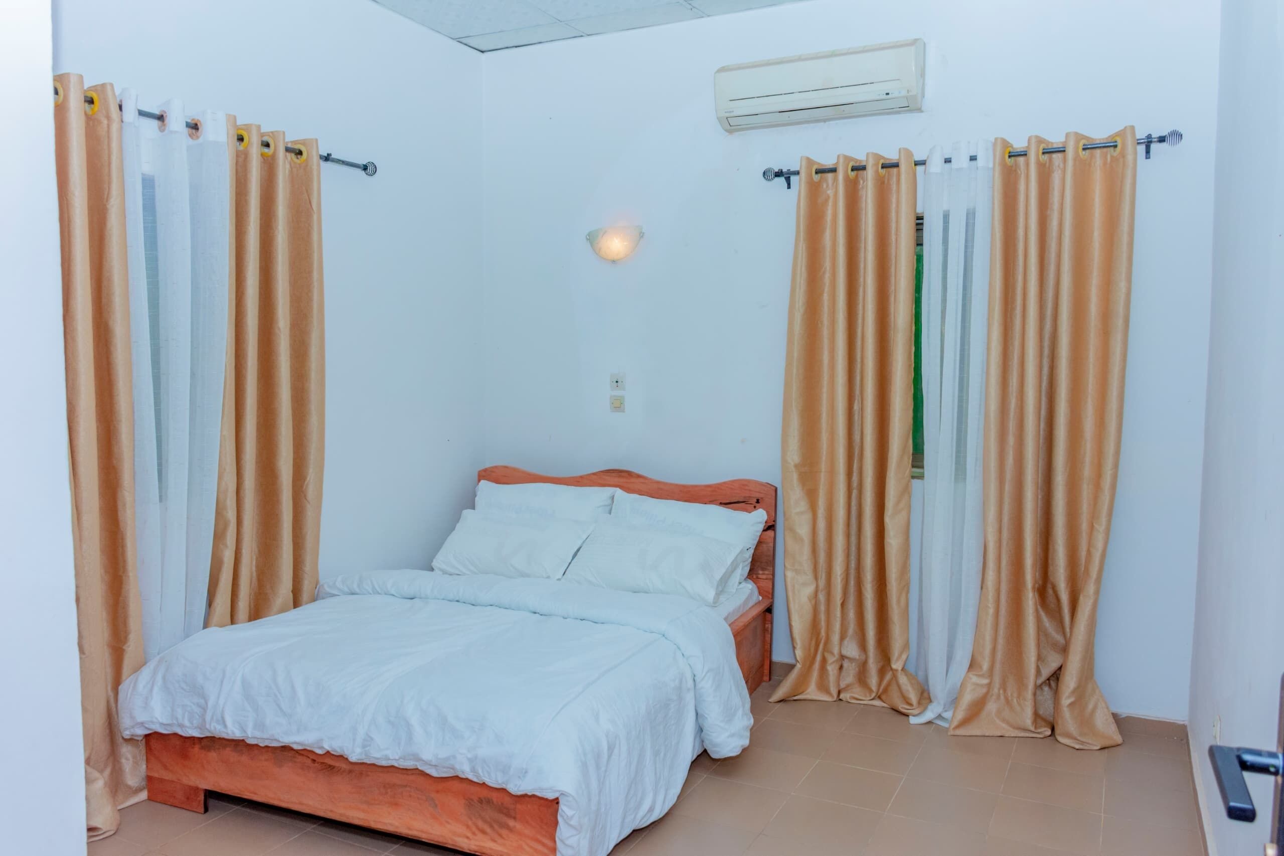 A bedroom with a bed, curtains, an air conditioning unit, and a wall-mounted light fixture.