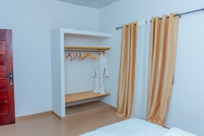 A room with a bed, a wooden shelf with hangers, and a white robe hanging on the wall.
