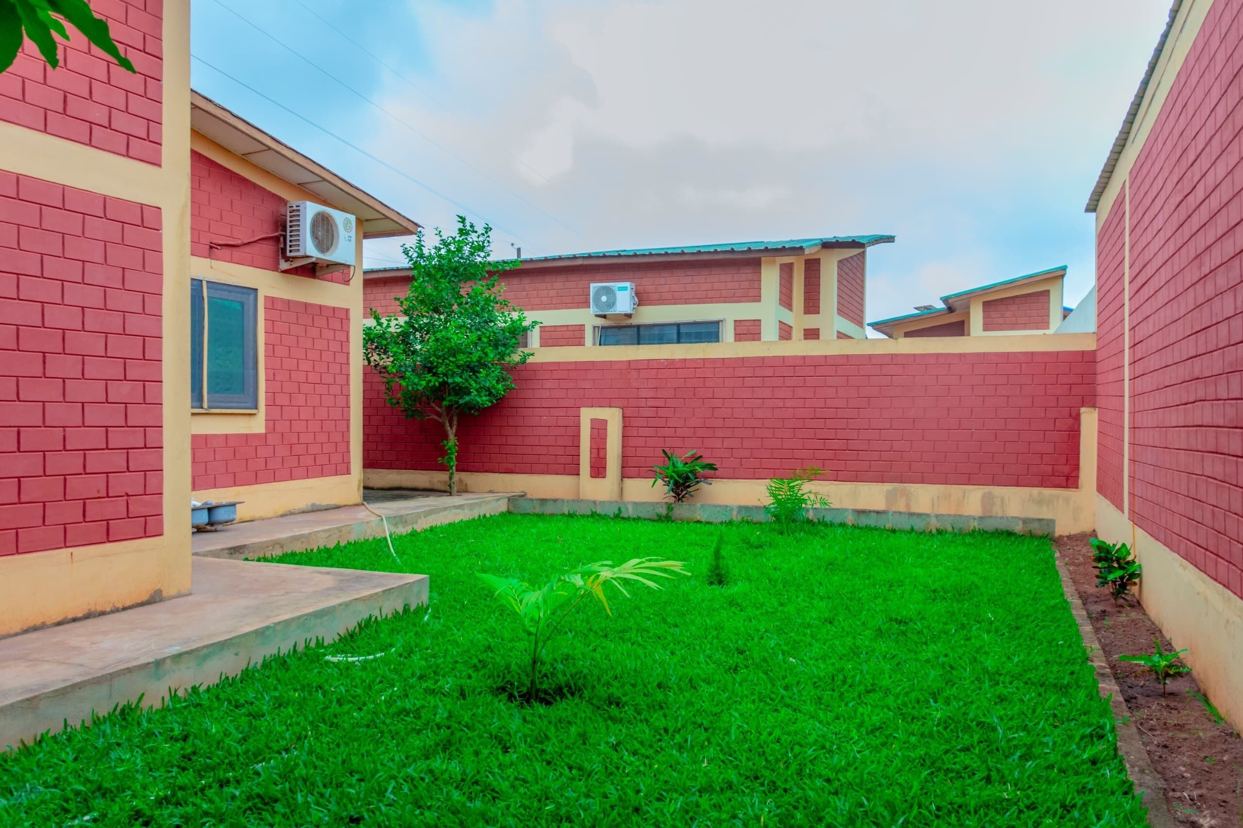 A courtyard with a well-maintained lawn, a small tree, and a building with red brick walls and beige trim.