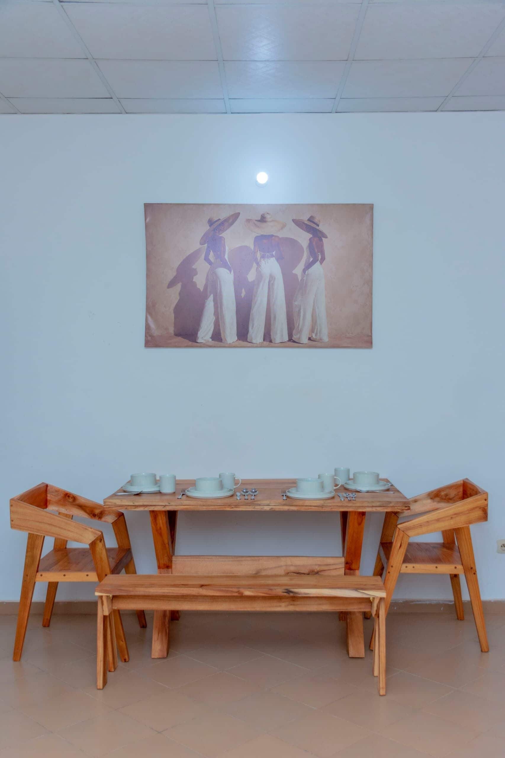 A dining area with a wooden table and chairs, a painting on the wall, and a ceiling light.