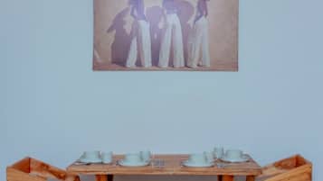 A dining area with a wooden table and chairs, a painting on the wall, and a ceiling light.