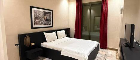 A hotel room with a bed, a television, a painting on the wall, and a patterned floor.