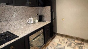 A kitchen with dark cabinets, a granite countertop, a stove, a refrigerator, and a patterned floor. - BELLA Palmeraie Apartment (Marrakech)