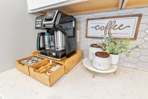 Een koffieapparaat op een aanrecht, met een bord met koffie-thema aan de muur en een houten doos met koffiecups.