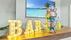En bardisk med upplysta bokstäver som bildar ordet ”BAR”, ett cocktailglas, en mixer och en flaska sprit placerade på en träyta.