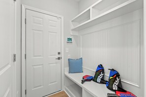 A white locker room with a door, a bench, and a wall-mounted thermostat. - Private Oasis • HotTub & Arcade! (North Myrtle Beach)