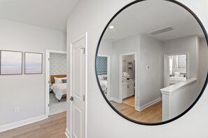 A modern bedroom with a large mirror, a bed with a wooden headboard, and a bathroom with a sink and mirror. - Private Oasis • HotTub & Arcade! (North Myrtle Beach)
