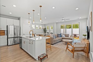Une cuisine moderne dotée d’un îlot central, d’appareils électroménagers en acier inoxydable, de luminaires suspendus et d’un coin repas avec un canapé et des chaises.