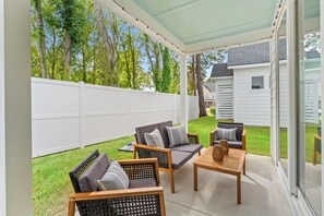 A covered patio area with outdoor furniture, a white fence, and a view of a house in the background. - Private Oasis • HotTub & Arcade! (North Myrtle Beach)