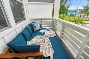 A covered outdoor seating area with a blue sofa, cushions, and a blanket. - Private Oasis • HotTub & Arcade! (North Myrtle Beach)