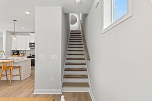 A modern kitchen with white cabinets, a wooden dining table, and a staircase leading to an upper level. - Private Oasis • HotTub & Arcade! (North Myrtle Beach)