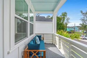 Un balcon avec un canapé bleu et une table en bois, donnant sur une rue bordée de voitures et de maisons.