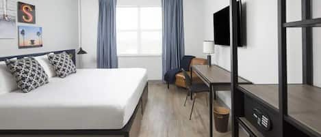 Ein Hotelzimmer mit Bett, Schreibtisch, Stuhl, Fernseher und einem Fenster mit Vorhängen.