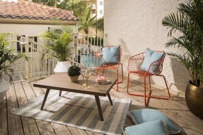 Eine Terrasse im Freien mit einem Holztisch, zwei Metallstühlen mit Kissen, einem Streifen Teppich und Topfpflanzen.