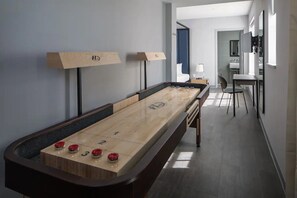 Une table de jeu de « shuffleboard » dans une chambre d’hôtel, avec vue sur le couloir et la salle de bain.
