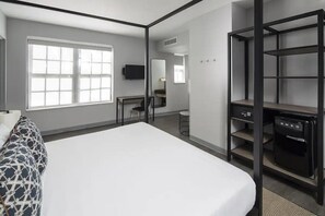 Une chambre d’hôtel moderne dotée d’un grand lit, d’un bureau, d’une chaise, d’une télévision, d’un miroir et d’une bibliothèque intégrée.