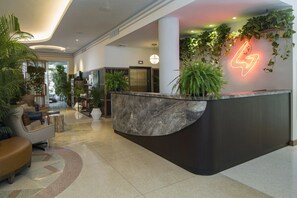 Un espace d’accueil moderne avec un comptoir en marbre, des plantes en pot et un panneau lumineux au néon.