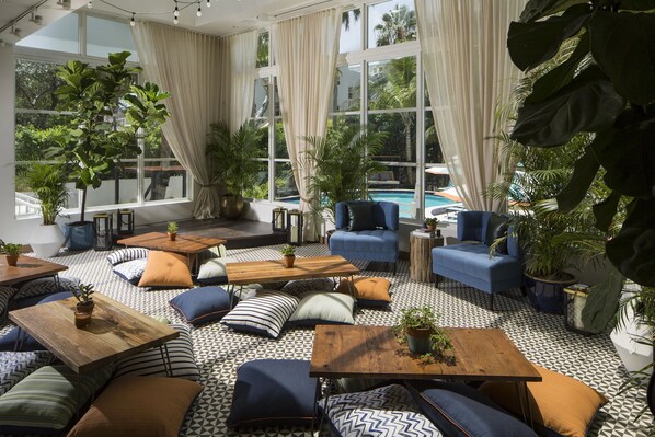 A spacious indoor area with multiple seating arrangements, large windows, and potted plants.