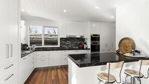 A modern kitchen with white cabinetry, a black countertop, and a large island with bar stools. - Barrambeet - Point Lonsdale (POINT LONSDALE)