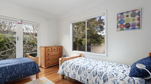 A bedroom with two beds, a dresser, a window, and a painting. - Bright Beach House - Point Lonsdale (POINT LONSDALE)