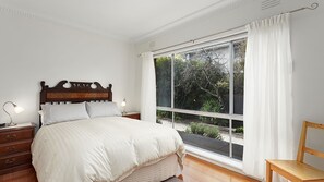 Quarto com uma grande janela, uma cama de madeira, abajures e uma cadeira de madeira.