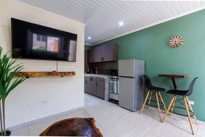 Eine moderne Küche mit Flachbildfernseher, Holzschränken, einem Kühlschrank und einem Essbereich mit zwei Stühlen.