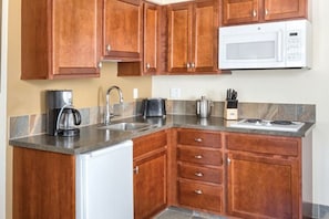 A kitchen with wooden cabinets, a white microwave, a coffee maker, and a stove.