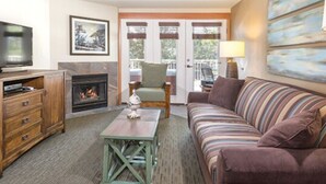 A living room with a television, fireplace, sofa, and a view of the outdoors through a glass door.