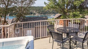 A hot tub on a wooden deck with a table and chairs, surrounded by a metal railing.