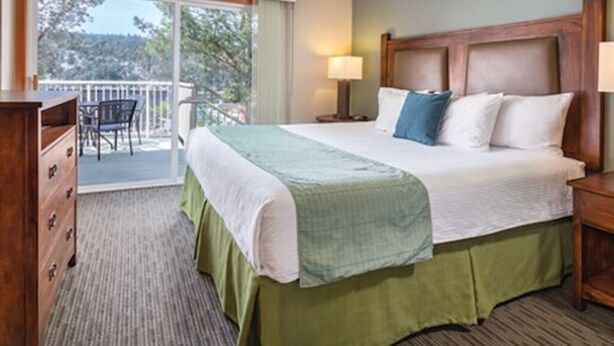 A hotel room with a bed, a dresser, a nightstand, a lamp, and a balcony with a chair.
