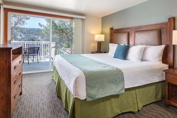 A hotel room with a bed, a dresser, a nightstand, a lamp, and a balcony with a chair.