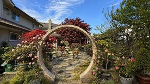 A garden with a stone archway, potted plants, and a variety of flowers. - Zen Garden Escape 2BR near YVR (Richmond)