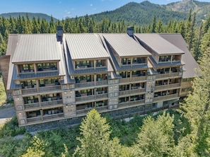 A multi-story lodge with balconies and large windows, surrounded by forested mountains. - Cloud Cap Condo 401 at South Grand Lodge | 2BR + Queen Loft, 3 Baths (Government Camp)