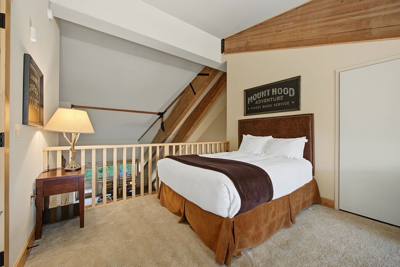 Ein Schlafzimmer mit einem Bett, einem Nachttisch, einer Lampe, einer Treppe und einem Schild mit der Aufschrift 'Mount Hood Adventure'.