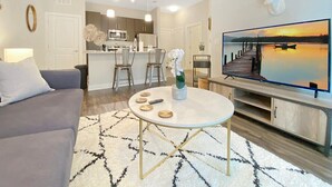 Una sala de estar moderna con un sofá gris, una mesa redonda de centro y un televisor de pantalla plana sobre un soporte de madera.