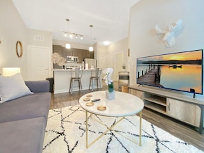 A modern living room with a grey sofa, a round coffee table, and a flat-screen TV on a wooden stand. - Upscale Living in Heart of Tampa, Courtyard Views (Tampa)