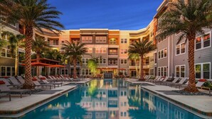 Un hotel con piscina central, varios pisos y palmeras.