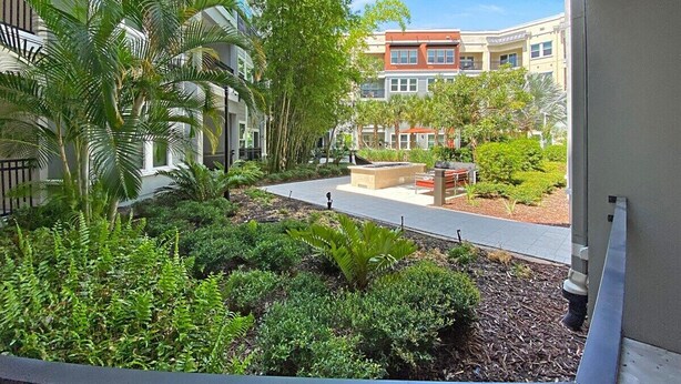 Un patio con un banco, una jardinera con plantas y un edificio de fachada roja al fondo.